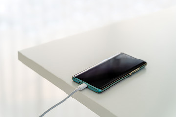 Mobile phone connected to charger power bank on white table.