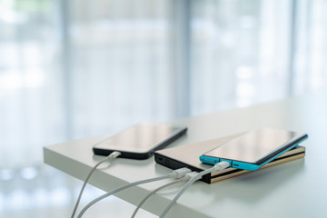 Mobile phone connected to charger power bank on white table.