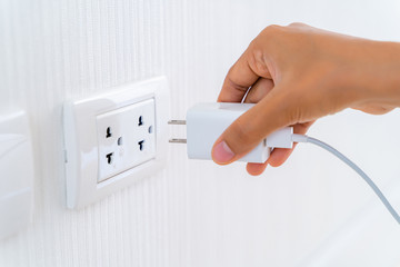 Woman's Hand Inserting Electrical Power Cord Plug into Receptacle on wall outlet.