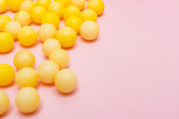 Yellow round dragees of vitamin c, ascorbic acid near a white plastic bottle, container on pink background