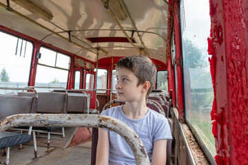 A 10 years boy riding in a old vintage bus, he is sad because his poor life and the bus moving going on a dirty country road