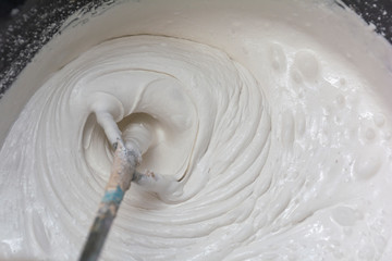 Building mixture in the process of preparation. A worker mixes the plaster in a bucket to level and putty the walls of the apartment with an electric drill, close-up.