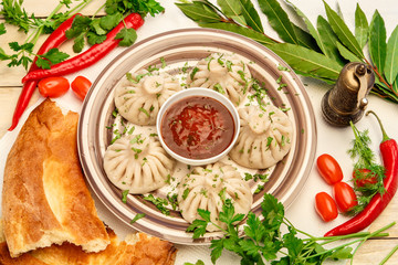 Georgian dumplings Khinkali with meat and parsley among vegetables and greens served tomato spicy sauce on a plate