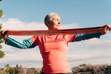 older woman with red t-shirt and elastic band practicing sport in the field