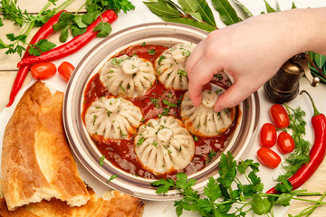 Georgian dumplings Khinkali with tomato spicy sauce on a plate among vegetables and greens