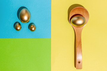Golden eggs in wooden spoons on a colorful background. Modern style.