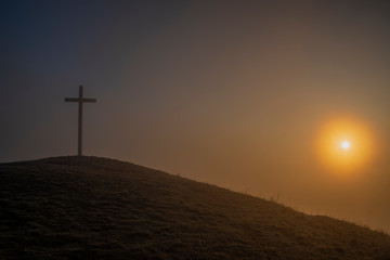 Sunrise on Radobyl hill with big cross and small statue in winter morning