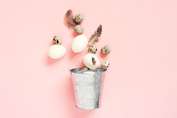 Easter eggs and feathers in the metal basket on pink background
