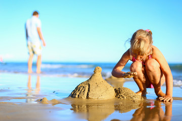 Cute little girl spend holidays in pink one-piece swimsuit, builds sand castle, plays in the water...