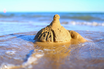 Sand castle in the water on the shore of the blue sea. Cute little girl spend holidays, plays and builds sculptures. Vacation with kids on beach on a warm sunny summer day before sunset