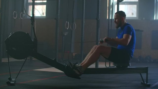 Slow motion men training rowing in gym with exercises machines and pull rope