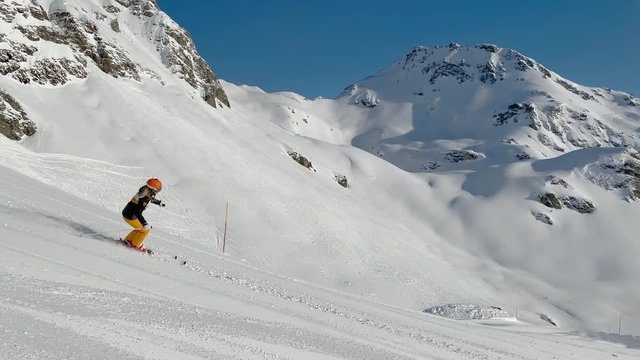 4K skiing footage, one woman skilled skier skiing on ski slope in long turns carving on sunny winter vacation day during ski holidays with clear blue sky high up in european alps mountains