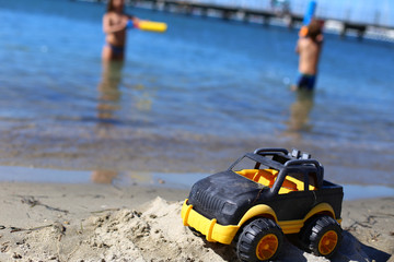 Children toy car jeep of black and yellow color on sand near the water on the beach of blue sea. Boys play water guns. Vacation with kids on coast on warm sunny summer day. Tourism in Europe,Slovenia