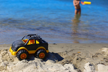 Children toy car jeep of black and yellow color on sand near the water on the beach of blue sea....