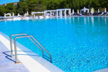 Ladder to go down to swimming pool on outdoor playgound zone of the hotel. Sunshine and clear blue water with sunny reflections. Summer holidays and vacation. Tourism in Europe, Slovenia, Portoroz