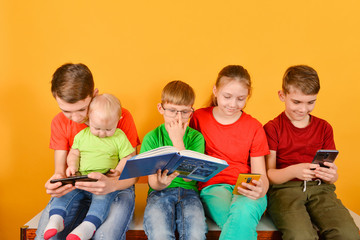 Children with a smartphone are sitting nearby, one boy in glasses is sitting with a book.