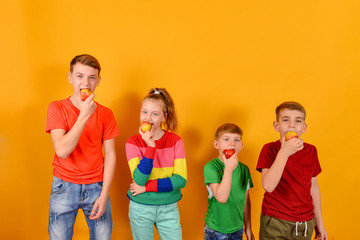 Four children eat an apple standing next to each other, guys on a yellow background in colorful color clothes.