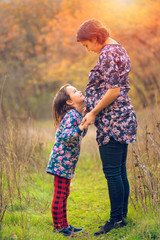 Happy family. Pregnant mom and little daughter hugging and kissing at sunset in autumn in forest. Laughter, happiness and fun together