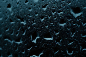 Texture of small and large drops on dark glass from rain on a green background