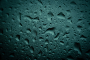 Texture of small and large drops on dark glass from rain on a green background