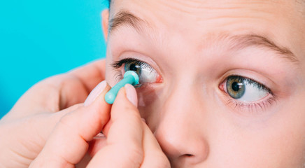 Optometrist trying on a contact lens to a teenage boy eye. Contact lenses for vision correction in children