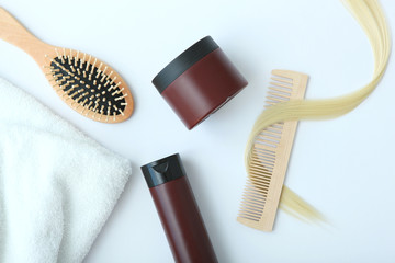A lock of blonde hair, hair care products and a comb on a colored background top view.