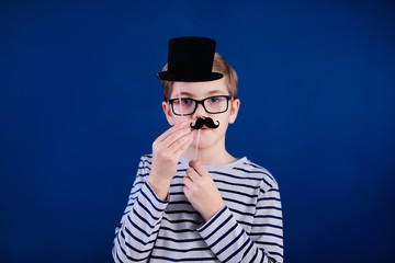 Birthday party and young boy with glasses in hats and props on blue background
