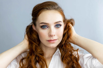 Ginger model with bright make-up and wavy hairstyle. Fashion highlighter on skin, sexy gloss lips, dark eyebrows. Posing on gray background, close up