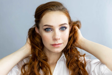 Fototapeta premium Ginger model with bright make-up and wavy hairstyle. Fashion highlighter on skin, sexy gloss lips, dark eyebrows. Posing on gray background, close up