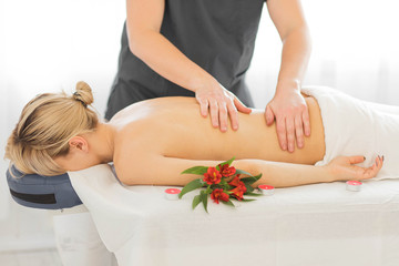 Hands of masseur ready for making massage. Blonde model smiling and lying on couch in private...