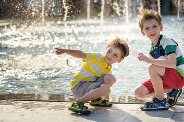 Cute toddler boy and older brothers, playing on a jet fountains with water splashing around, summertime