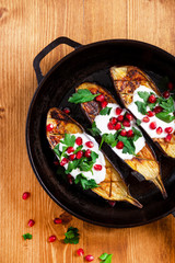 Grilled eggplant with yogurt, pomegranate and parsley in a pan on a wooden background, top view. Tasty and healthy Mediterranean cuisine.