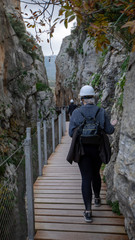 Woman crossing a narrow pass through rocks hills and wearing a white helmet.