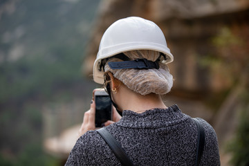 White woman holding her phone and taking a picture of a landscape. wearing a white helmet.