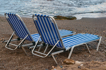 Fototapeta premium sun loungers on a pebble beach of the Greek resort town of Hersonissos on a background of blue sea