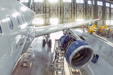 A working mechanic is repairing a passenger plane engine in a hangar.