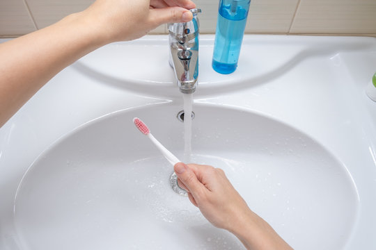 Female hands washing a toothbrush in the bathroom, dental care concept and preparation for teeth cleaning