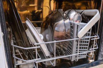 Open overloaded dishwasher with different dishes and kitchen utensils