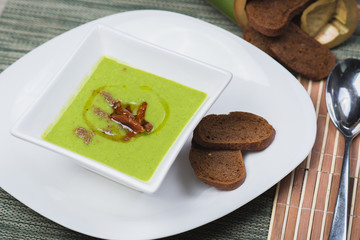 Green vegetarian broccoli cream soup with rye crackers on a wooden table in a restaurant or cafe.