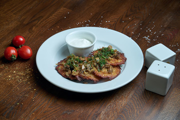 Close up view on Traditional dish of Ukrainian cuisine - potato pancakes with sour cream and mushroom on a white ceramic plate on rustic background