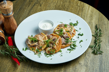 Close up view on Traditional dish of Ukrainian cuisine - potato pancakes with sour cream and beef on a white ceramic plate on rustic background