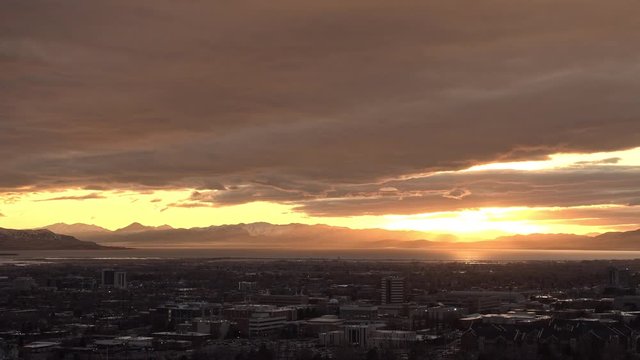 Sun rays shining through clouds over Utah Lake past Provo city during sunset.