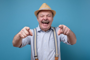 Joyful senior hispanic man pointing at you laughing. Funny joke or prank concept. - obrazy, fototapety, plakaty