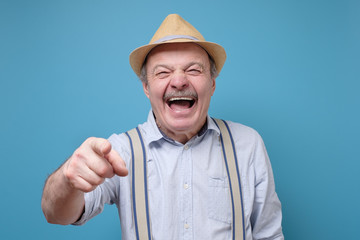 Joyful senior hispanic man pointing at you laughing. Funny joke or prank concept.