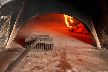 Pizza Chef cleaning pizza oven with special brush. Traditional wood oven in restaurant, Italy....