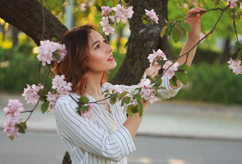 A woman dressed in fashionable leather trousers and a white tree with a blossoming apple tree.