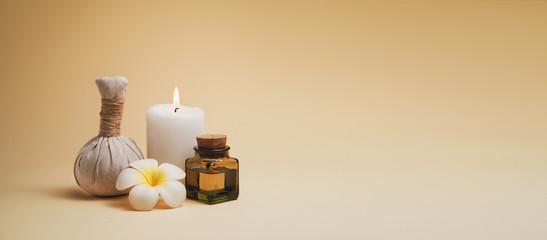 Beautiful spa composition with candle, frangipani flower, oil flask and herbal ball on beige background. Stylized warm colors and contrast. Copy space