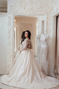 Full length photo of bride in wedding shop. Woman posing near mirror.  Gorgeous bride in luxury wedding dress. Wedding make up and hairstyle, wedding jewelry.