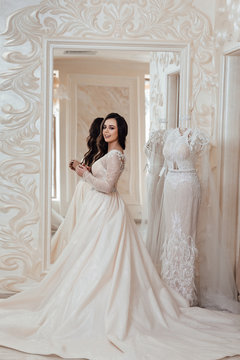 Full length photo of bride in wedding shop. Woman posing near mirror.  Gorgeous bride in luxury wedding dress. Wedding make up and hairstyle, wedding jewelry.