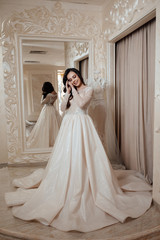 Wedding fashion and beauty salon. Woman posing near mirror. Fashion model or princess at prom. Sexy girl in white dress with stylish hair. Full length photo of bride in wedding shop.